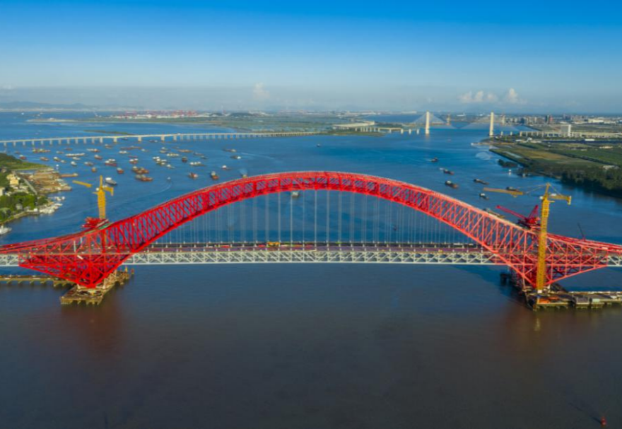 明珠灣大橋位于廣州市南沙區(qū)龍穴南水道之上，是粵港澳大灣區(qū)的重要連接通道。大橋工程全長約10.42公里，主線全長約9.1公里，主橋采用中承式六跨連續(xù)鋼桁拱橋，全長1016米，為同類型橋梁最大跨度。氣勢恢宏的明珠灣大橋綿延伸向遠方，將南沙多條核心主干道緊緊連在一起，構(gòu)筑了明珠灣區(qū)內(nèi)部核心交通環(huán)，是廣州面向粵港澳大灣區(qū)建設(shè)的交通樞紐工程和地標性建筑。圖為南沙明珠灣大橋。