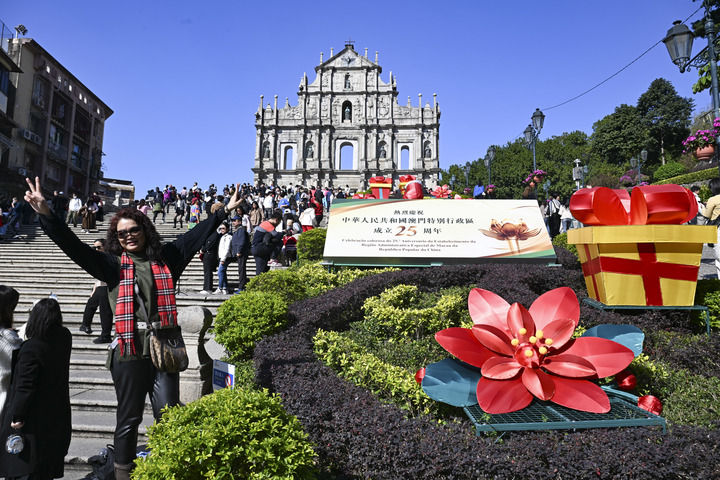游客在澳門(mén)大三巴牌坊慶祝布景旁留影（2024年12月18日攝）。新華社記者 程一恒 攝
