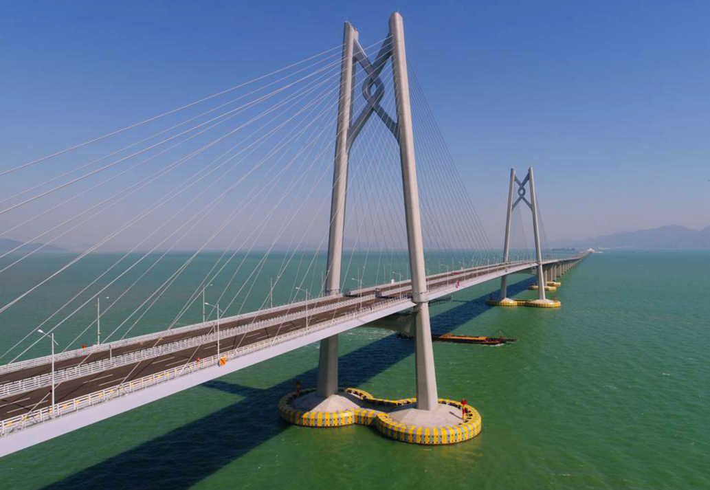 港珠澳大橋主體工程實(shí)行橋、島、隧于一體，總長(zhǎng)約29.6公里，穿越伶仃航道和銅鼓西航道段約6.7公里為隧道，東、西兩端各設(shè)置一個(gè)海中人工島（藍(lán)海豚島和白海豚島），猶如“伶仃雙貝”熠熠生輝；其余路段約22.9公里為橋梁，分別設(shè)有寓意三地同心的“中國(guó)結(jié)”青州橋、人與自然和諧相處的“海豚塔”江海橋，以及揚(yáng)帆起航的“風(fēng)帆塔”九洲橋三座通航斜拉橋。圖為寓意三地同心的“中國(guó)結(jié)”青州橋。